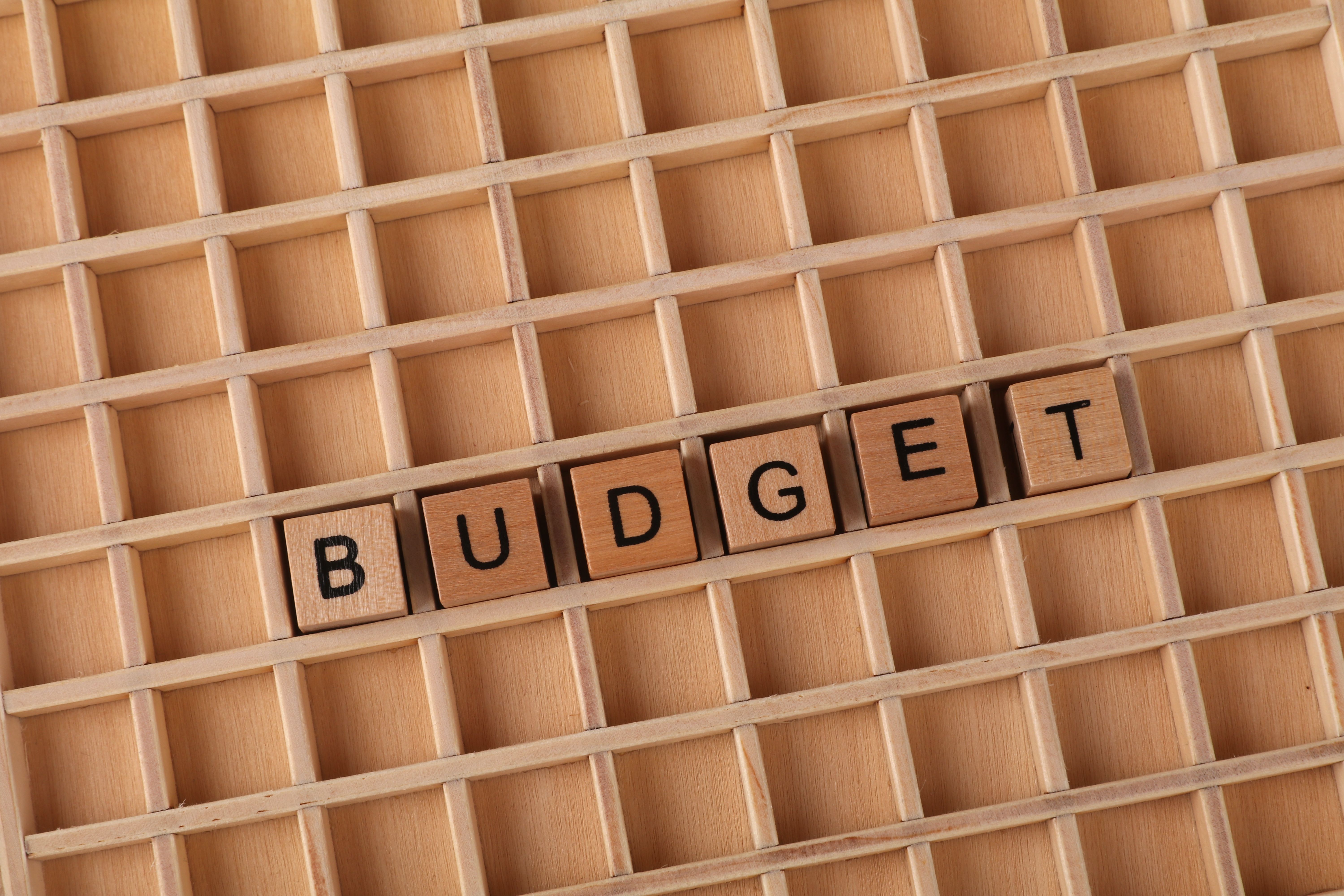 Wooden letter tiles spelling 'budget' on a grid background symbolizing financial planning