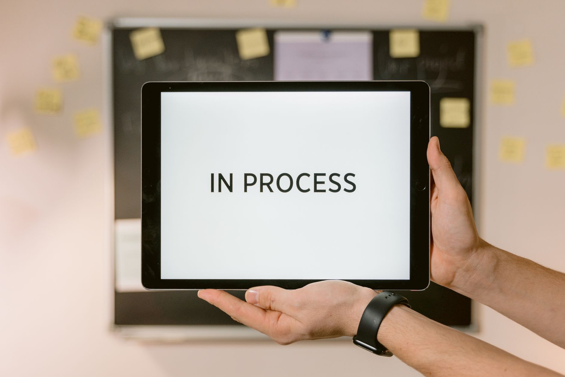Close-up of hands holding a tablet displaying 'In Process' text, emphasizing workflow.
